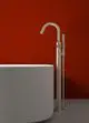Freistehende Badarmatur in silberner Ausführung, platziert neben einer runden Badewanne, vor einer roten Wand. Produkt von Ideal Standard.
